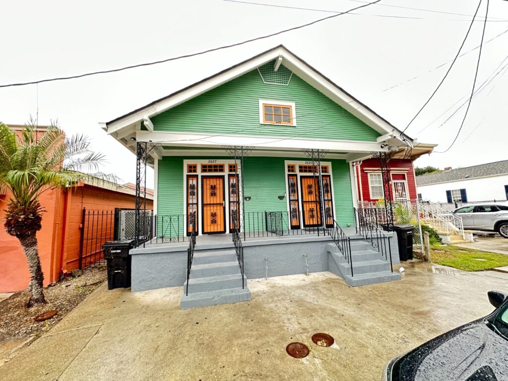 A vibrant green New Orleans investment property with ornate ironwork and orange doors, highlighting DuCar Construction's real estate offerings.