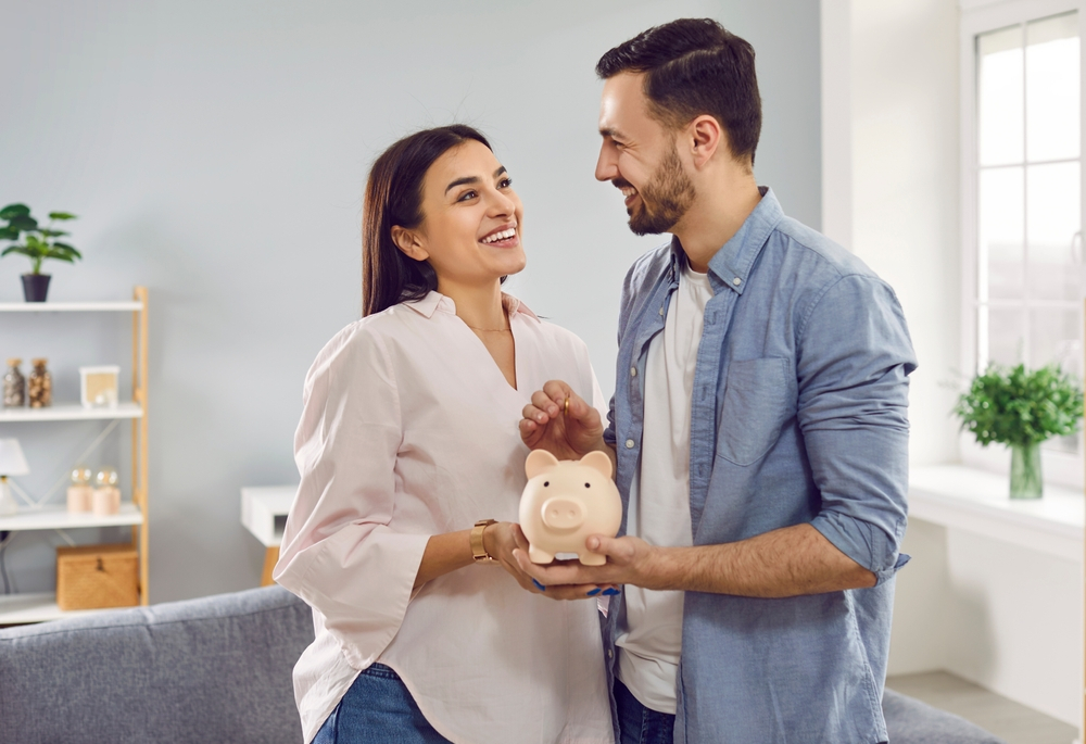 Married couple smiling while holding their finances - real estate investment house hacking