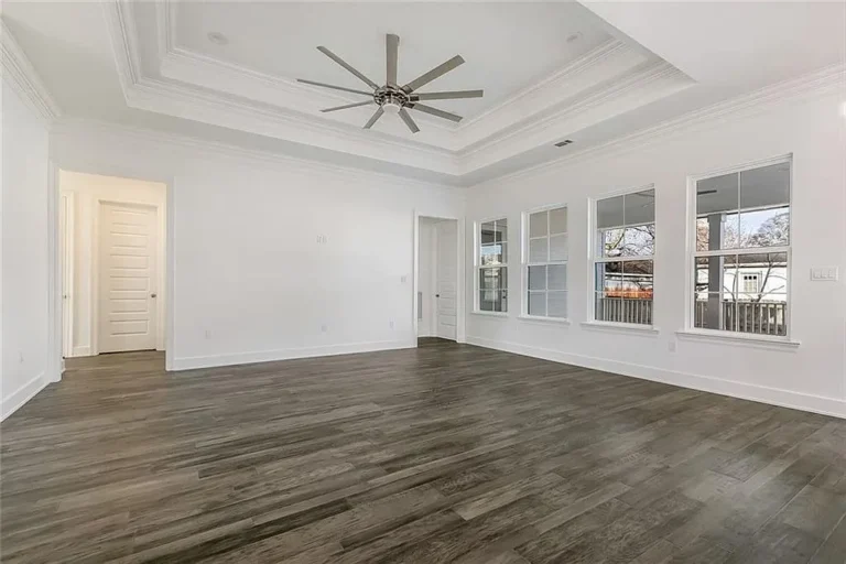 Primary bedroom with a tray ceiling and windows onto the back porch in a DuCar new home in New Orleans