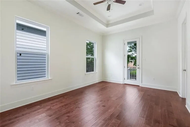 Primary bedroom with a tray ceiling and a door to a private porch in a DuCar new home in New Orleans